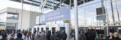 Numerous visitors enter the entrance hall of productronica through the revolving doors of the Messe München main entrance.