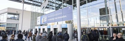 Zahlreiche Besucher betreten die Eingangshalle der productronica durch die Drehtüren des Messe München Haupteingangs.