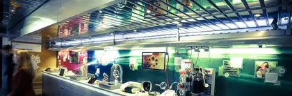 Ein modernes Labor mit verschiedenen wissenschaftlichen Geräten auf einer langen Arbeitsfläche, beleuchtet von blau-grünen Lichtern. Im Hintergrund sind Bildschirme und Spiegel zu sehen.