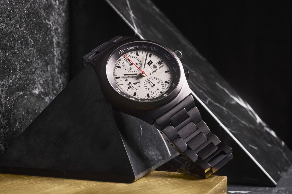Eine schwarze Armbanduhr mit weißem Zifferblatt und Chronograph wird auf einer schwarzen Marmorpyramide präsentiert.