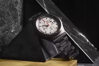 Eine schwarze Armbanduhr mit weißem Zifferblatt und Chronograph wird auf einer schwarzen Marmorpyramide präsentiert.