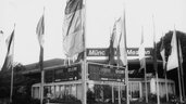 Black and white photo of flags and signs in front of the entrance to the LASER 83 trade fair.