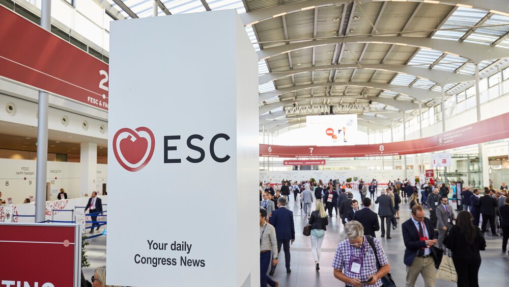 Blick in eine hohe Halle mit gewölbtem Dach während des ESC Congress mit zahlreichen Besuchern, die in unterschiedliche Richtungen laufen.