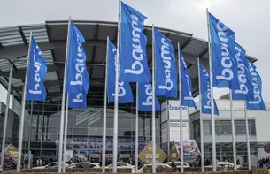 Bauma flags in front of a modern glass building, the entrance to the Messe München exhibition centre.