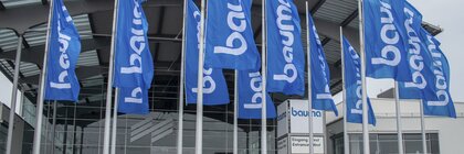 Bauma-Flaggen vor einem modernen Glasgebäude, dem Eingang zum Messegelände München.