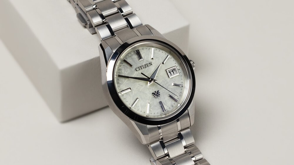 A close-up view of a wristwatch with a milky dial displaying the day of the week and a delicate silver bracelet.