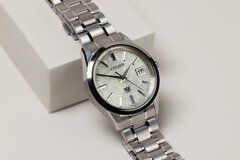 A close-up view of a wristwatch with a milky dial displaying the day of the week and a delicate silver bracelet.