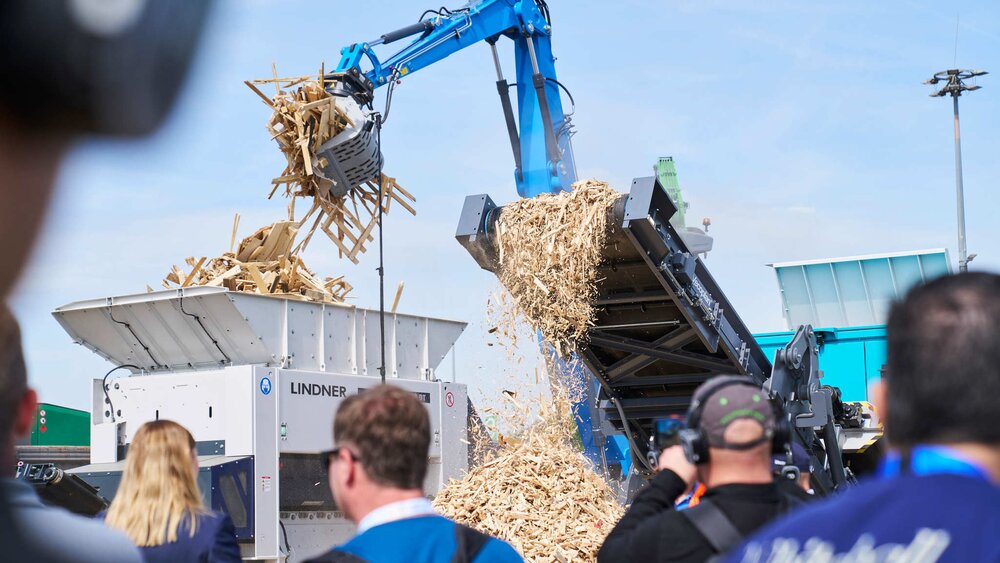 Mobile Lindner shredder processing waste wood at the IFAT outdoor area, observed by spectators.