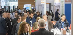 Eine gut gefüllte Ausstellungshalle mit interagierenden Besuchern und einer Gruppe die um einen einem Stand steht.