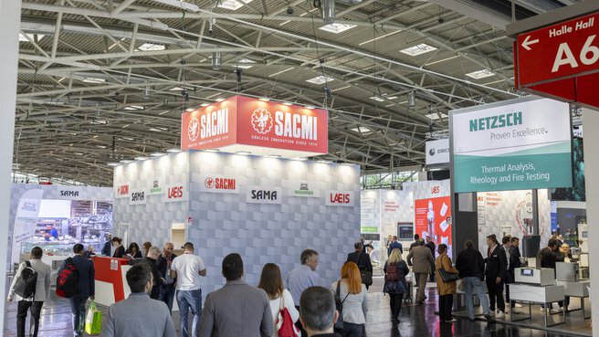 A busy exhibition hall with people visiting the various brightly lit stands and exhibitions.