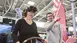 A woman tries out VR glasses at an exhibition stand and holds a steering wheel in her hand. On the right is a man explaining the experience to her.