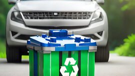 Green recyclable battery on the street with a blurred car in the background.