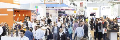 Gut frequentierte Messehalle A2, mit Besuchern, die an verschiedenen Ständen und Ausstellungen der Industrie vorbeigehen.