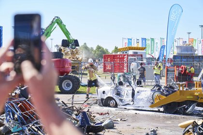 A worker sprays a destroyed vehicle with foam during a demonstration in the outdoor area. Debris can be seen all around.