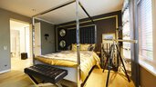 Modernes Schlafzimmer mit goldakzentuiertem Dekor, Himmelbett, Teleskop am Fenster und Kunstwerken an der Wand.
