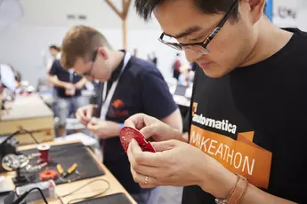 Zwei Personen arbeiten bei einem Maker-Event an Elektronikprojekten und nehmen Leiterplatten genau unter die Lupe.