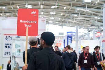 Tourguide mit Rundgang-Schild in der Messehalle