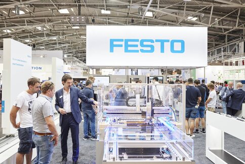 People gather around a machine at an exhibition stand with a large FESTO sign above their heads.