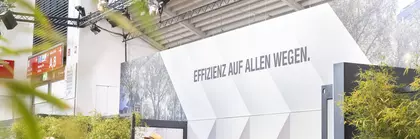 Menschen versammelten sich um Tische an einem Messestand. Im Hintergrund ist eine Kaffeebar und ein großes Schild mit der Aufschrift „Effizienz auf allen Wegen“.