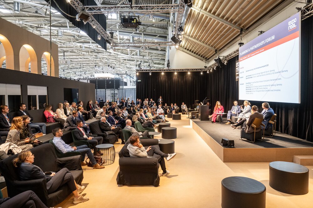 A comfortably seated audience follows a panel discussion of 5 people on the stage of the Planning & Partnerships Forum at EXPO REAL.