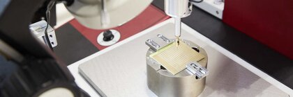 Bild einer Präzisionsfräse unter der eine kleine Quadratische Platte mit eingefrästen Mustern eingespannt ist.