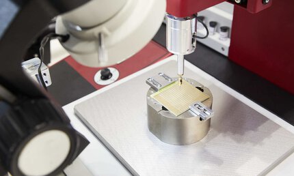 Bild von der productronica, eine Nahaufnahme eines Messtasters, der über einer fixierten Plakette schwebt.