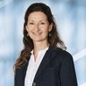 Lächelnde Frau mit langen dunklen Haaren und grünen Ohrringen, mit Jackett und weißem Hemd.
