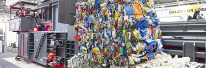 Three stacked bales of colorful, compacted recycling materials in front of an industrial baler.
