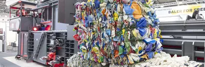 Drei gestapelte Ballen mit bunten, verdichteten Recyclingmaterialien vor einer industriellen Ballenpresse.