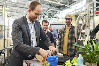A man demonstrates how to use a device in front of two visitors at an exhibition stand.