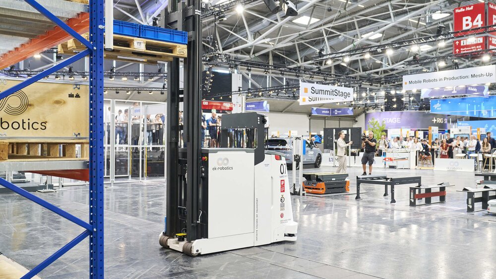 Autonomous transport vehicle in an exhibition hall with shelving and other robots.
