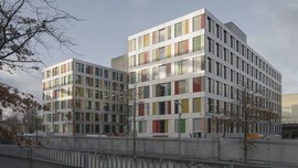 Ein großes modernes Bürogebäude mit rechteckigen bunten Elementen in Rot, Grün und Gelb zwischen den Fenstern.