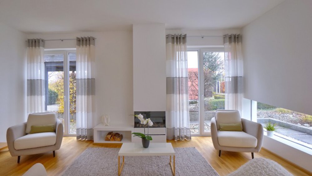 Minimalistisches Wohnzimmer mit Sesseln, Couchtisch und großen Fenstern, die Tageslicht hereinlassen.