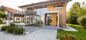 Modernes zweistöckiges Haus mit großen Glasfenstern, einem Steinweg und Grünflächen im Vorgarten.