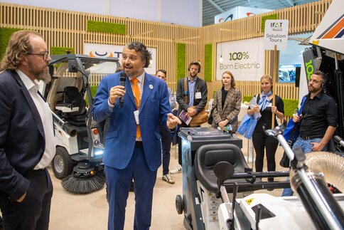 An exhibitor informs a group of visitors about modern drive concepts for municipal machines and vehicles during an IFAT Munich solution tour