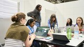 Eine Gruppe junger Frauen arbeitet konzentriert an Laptops während eines Workshops auf der World of Quantum 2025 in München.