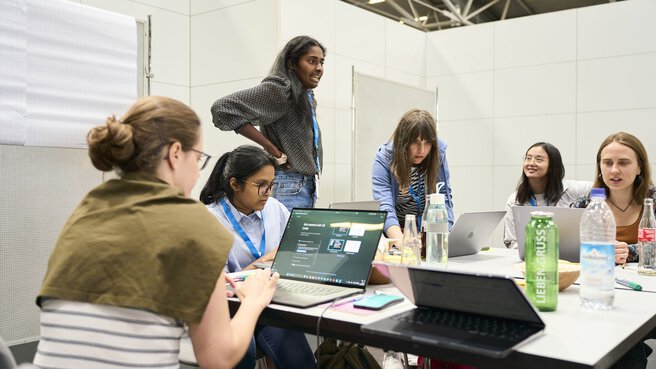 Eine Gruppe junger Frauen arbeitet konzentriert an Laptops während eines Workshops auf der World of Quantum 2025 in München.
