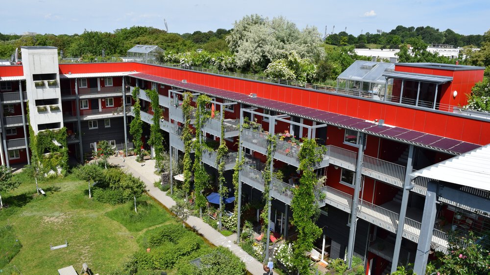  Green roofs and facades of various residential and building complexes, surrounded by lush vegetation and urban greenery, as examples of sustainable architecture and nature-oriented urban design.