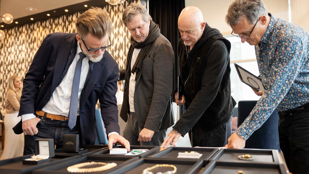 Four men examine pieces of jewellery on display tables in a showroom.