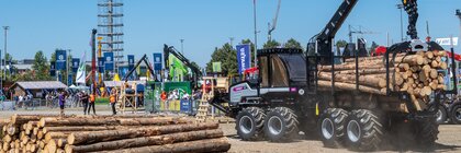 Forstmaschine lädt Baumstämme auf einem Vorführgelände, während Besucher eine Demonstration auf einer Fachmesse beobachten.