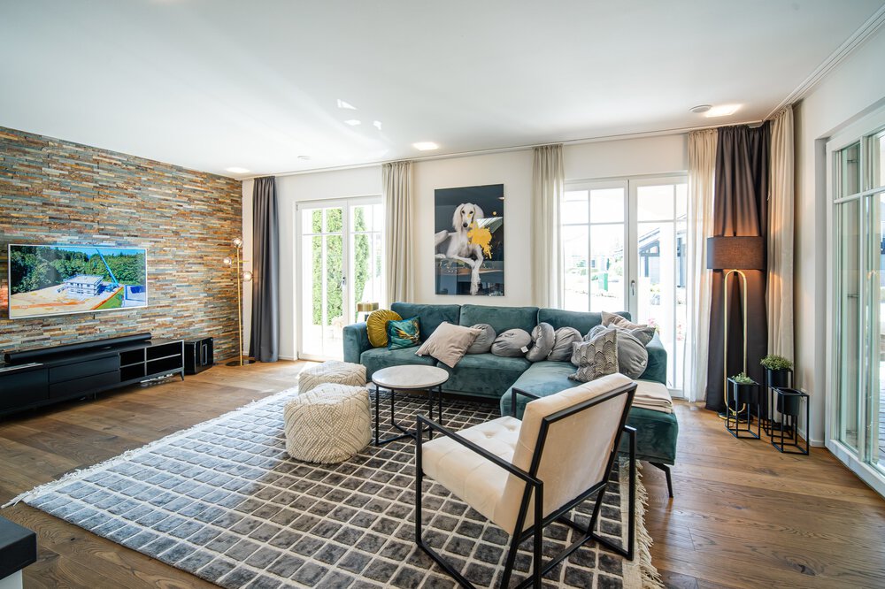 Stilvolles Wohnzimmer mit grünem Sofa, Fernseher, Akzentwand aus Stein, modernem Dekor, großen Fenstern und hellem Holzboden.