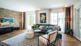 Stilvolles Wohnzimmer mit grünem Sofa, Fernseher, Akzentwand aus Stein, modernem Dekor, großen Fenstern und hellem Holzboden.