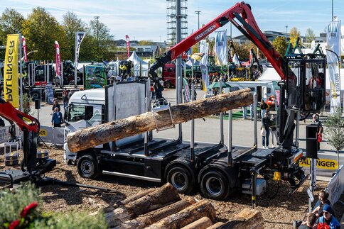 Forestry crane lifting a tree trunk onto a logging truck in an outdoor exhibition area.