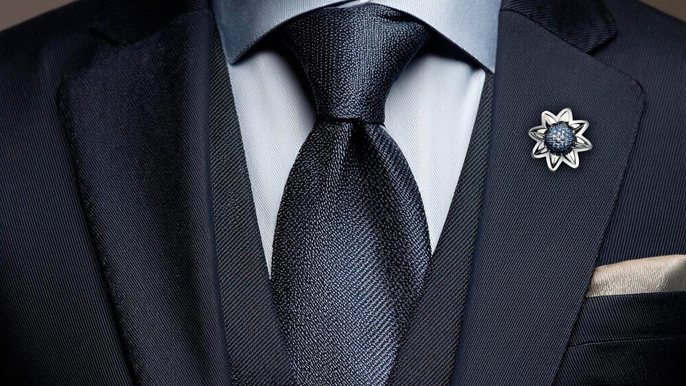 Close-up view of a silver flower brooch on the lapel of a black suit with a black tie in the center.