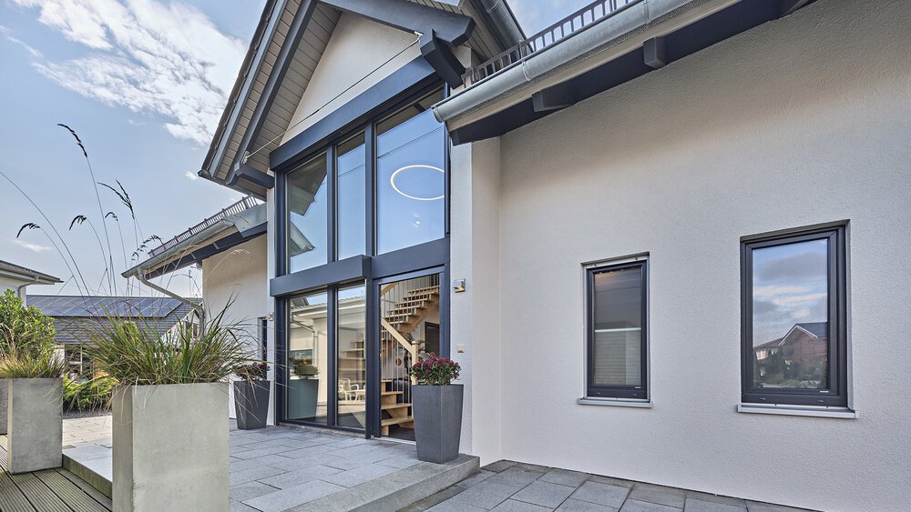 Vor diesem modernen KAMPA-Haus stehen üppige Topfpflanzen und ein gepflasterten Gehweg führt zum einladenden Eingangsbereich mit verglastem Quergiebel.