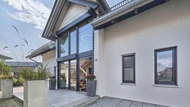 Vor diesem modernen KAMPA-Haus stehen üppige Topfpflanzen und ein gepflasterten Gehweg führt zum einladenden Eingangsbereich mit verglastem Quergiebel.