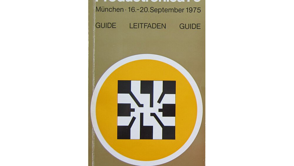 A catalogue for productronica 1975 in brown. In the centre is a black and white square in a yellow circle with a white border.