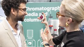 Ausstellerin erklärt einem Besucher ein Produkt auf einer Labortechnik-Messe.