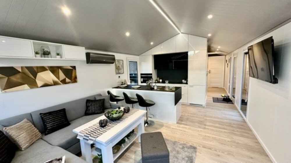 Modernes offenes Wohnzimmer und Küche mit eleganten Möbeln, einem Sofa, Barhockern und zeitgenössischem Dekor.