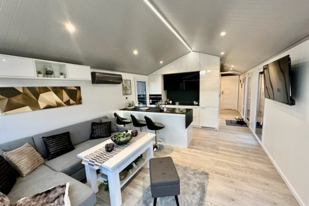 Modernes offenes Wohnzimmer und Küche mit eleganten Möbeln, einem Sofa, Barhockern und zeitgenössischem Dekor.